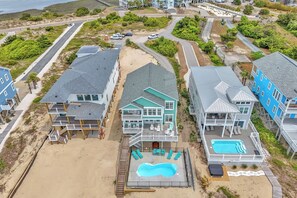 A beachfront property with a swimming pool, multiple decks, and a view of the ocean.