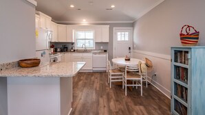 A modern kitchen with white cabinets, a granite countertop, and a dining area with a white table and chairs.