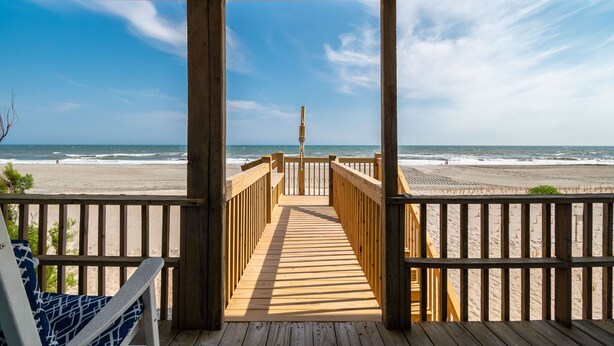 A wooden deck leading to a beach with a clear view of the ocean.