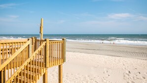 A wooden beach deck with a railing overlooking a sandy beach and the ocean.