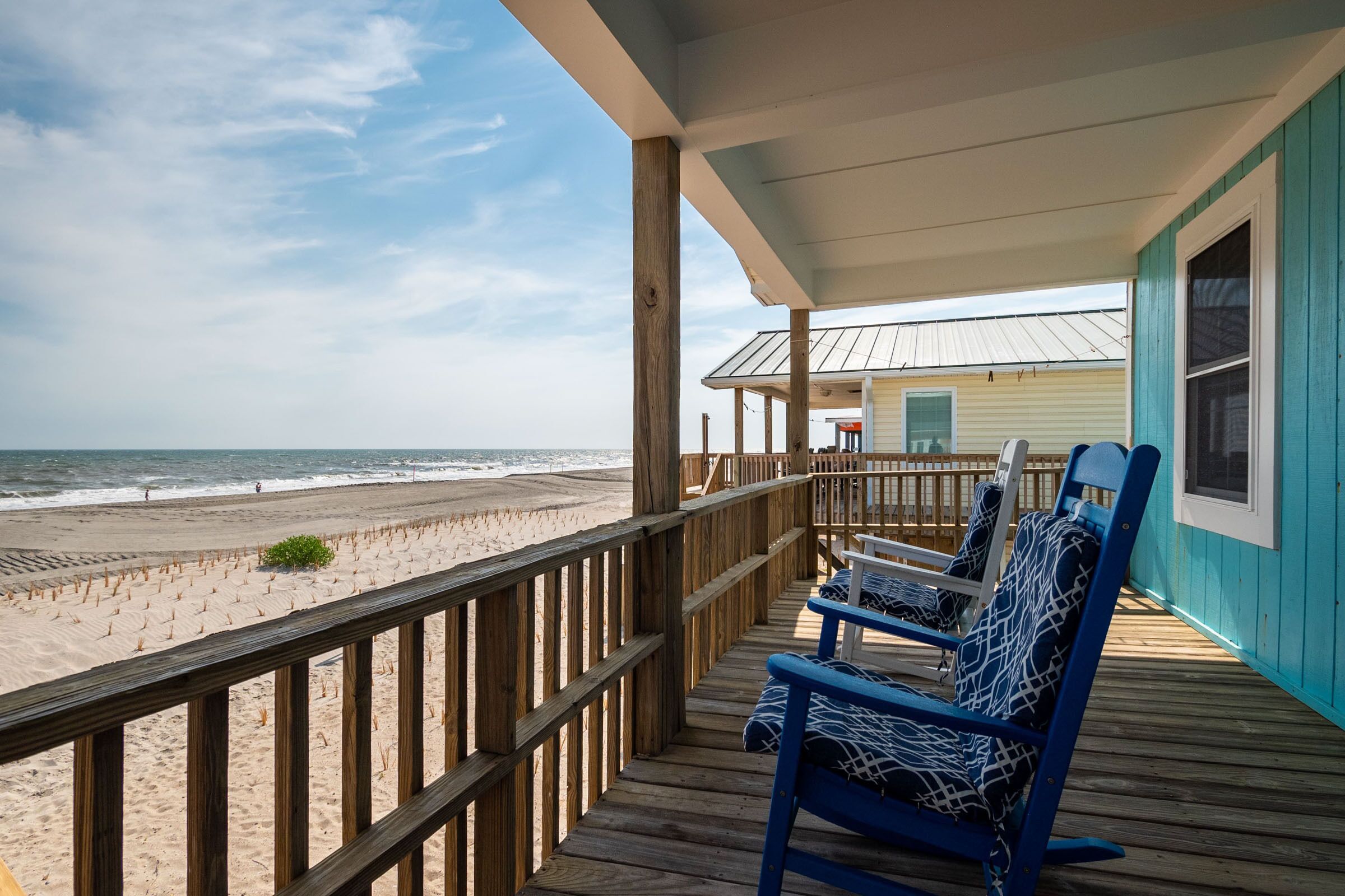 A wooden deck with blue chairs overlooking a beach.