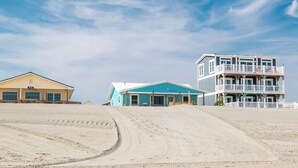 A beachfront property with a sandy beach, a blue building with a balcony, and a multi-story building with a white fence.