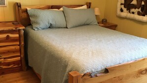 A wooden bed with a quilt, a wooden nightstand, a lamp, and a welcome sign on the wall.