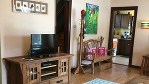 A living room with a wooden entertainment center, a television, a patterned rug, and a dining area with a wooden table and chairs.