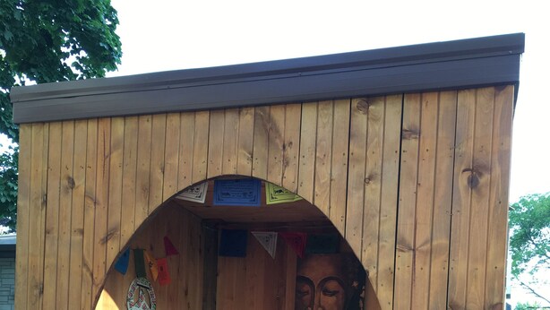 A wooden structure with a semi-circular archway, a cushioned bench, and a small table.
