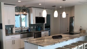 A modern kitchen with white cabinetry, a marble countertop, and a central island with bar stools. - Decompress and Revitalize! Lose yourself in Paradise! (Fort Myers Beach)