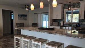 A modern kitchen with a central island, bar stools, pendant lighting, and a herringbone-patterned backsplash. - Decompress and Revitalize! Lose yourself in Paradise! (Fort Myers Beach)