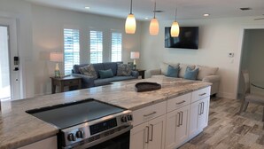 A modern kitchen with a large island, built-in oven, and stainless steel appliances. There is a seating area with a sofa and a TV mounted on the wall. - Decompress and Revitalize! Lose yourself in Paradise! (Fort Myers Beach)