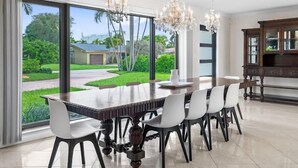 Comedor con una mesa grande, sillas y vistas a un jardín exuberante a través de amplios ventanales.