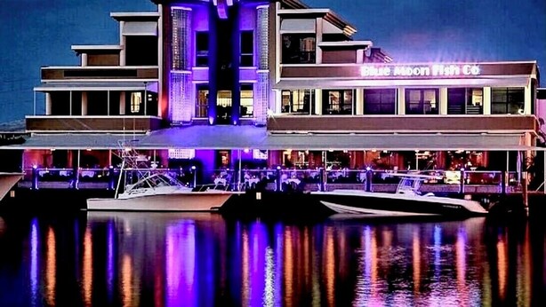 Un edificio frente al agua con un letrero que dice "Blue Moon Fish Co." y un muelle con barcos.