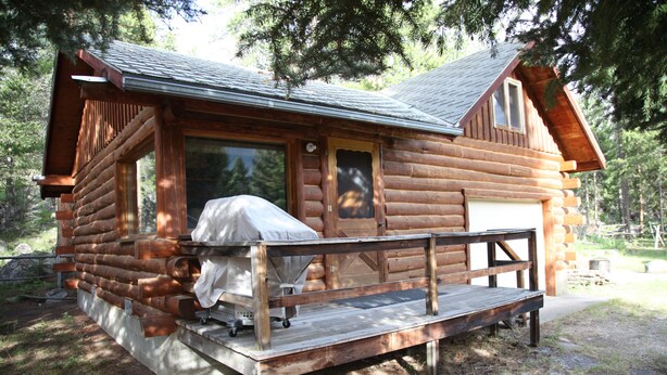 Una baita di legno con una terrazza in legno e un'area salotto esterna coperta.