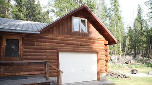Una baita di legno con un portone garage bianco, un patio in legno e un piccolo portico.
