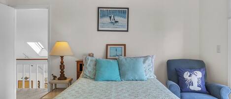 A bedroom with a bed, a chair, a lamp, and a painting on the wall.