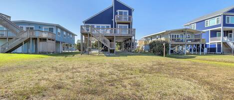A beachfront property with multiple levels, outdoor decks, and a grassy lawn.