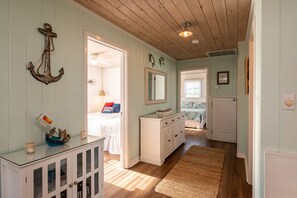 Une pièce avec un plafond en bois, une armoire blanche avec des portes en verre, un lit recouvert d’une courtepointe blanche et un miroir au-dessus de l’armoire.