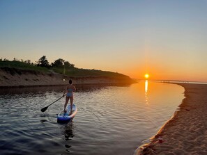 A person paddleboarding on a calm river at sunset.