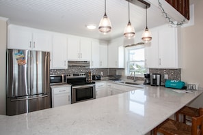 Una cocina moderna con gabinetes blancos, electrodomésticos de acero inoxidable, una isla grande e iluminación colgante.