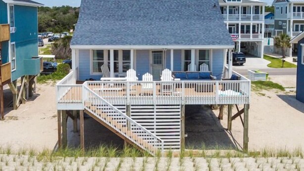 Une maison située en bord de mer, dotée d’un porche couvert, d’un escalier menant à une terrasse et offrant une vue sur la plage.