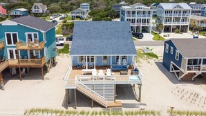 Une propriété située en bord de mer, comprenant une grande maison dotée d’un patio couvert, d’une terrasse et d’un escalier menant à un deuxième étage.