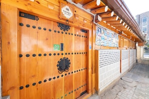 A wooden door with a sign above it, a brick wall, and a tiled floor. - Open Real Luxury Korean Hanok (Seoul)