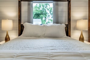 A bed with a white bedspread, two bedside lamps, and a window with a view of trees.