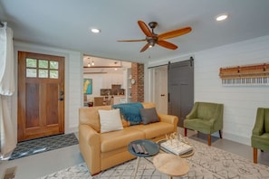 A living room with a sofa, two chairs, a coffee table, a ceiling fan, and a door leading to a kitchen.