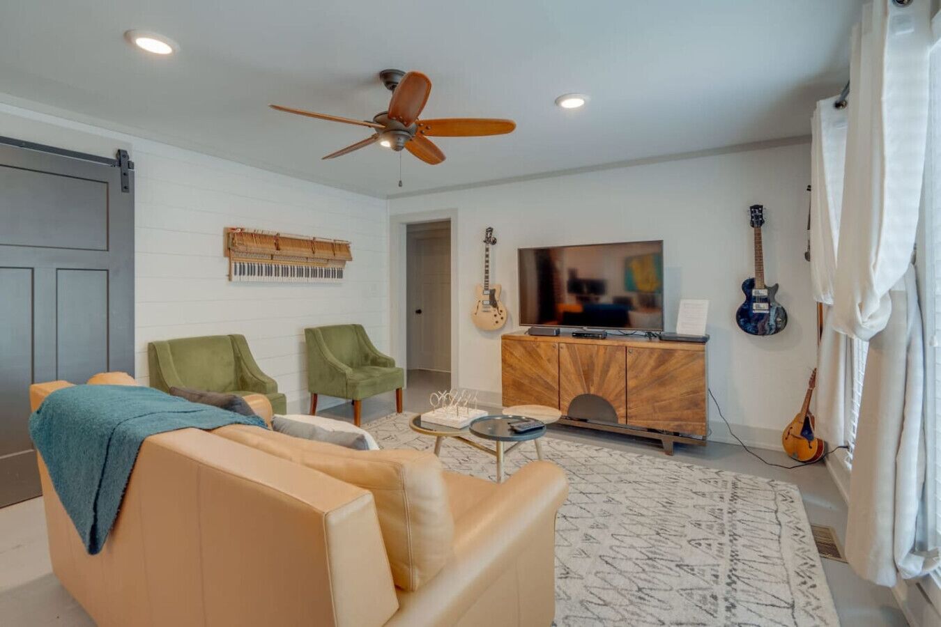 Una sala de estar con sofá, dos sillones, televisión, guitarra y ventilador de techo.