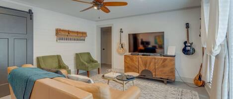 Una sala de estar con sofá, dos sillones, televisión, guitarra y ventilador de techo.