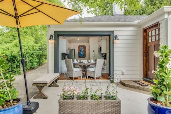 A covered patio with a table and chairs, a yellow umbrella, and potted plants.