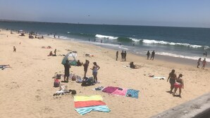Una platja amb gent que pren el sol, nedant i passejant al llarg de la riba.