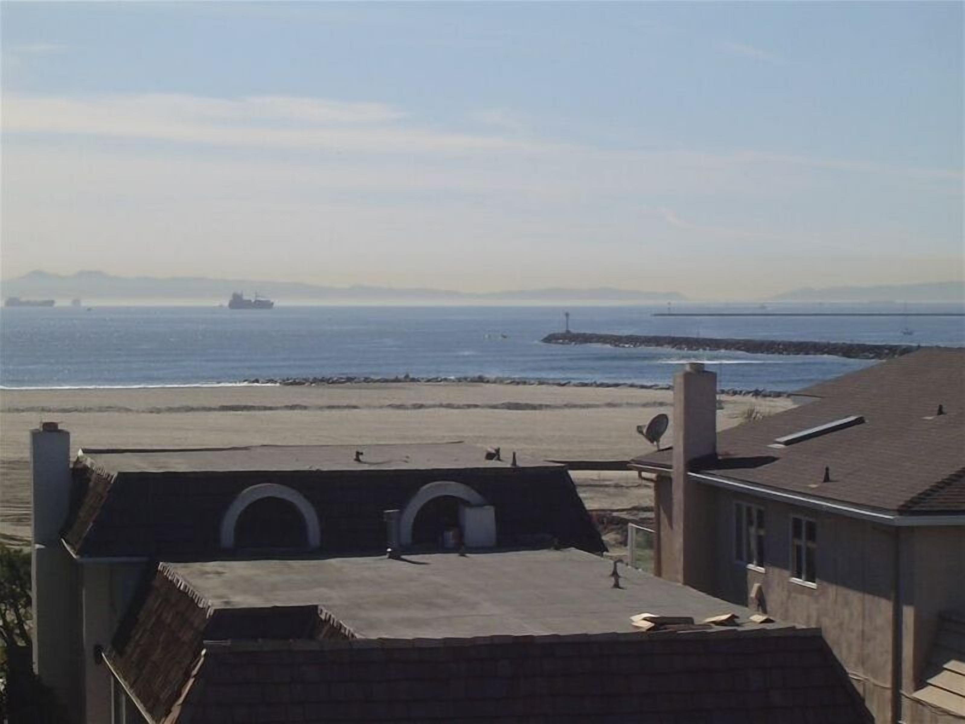 A coastal view with a beach, a pier, and a ship in the distance.