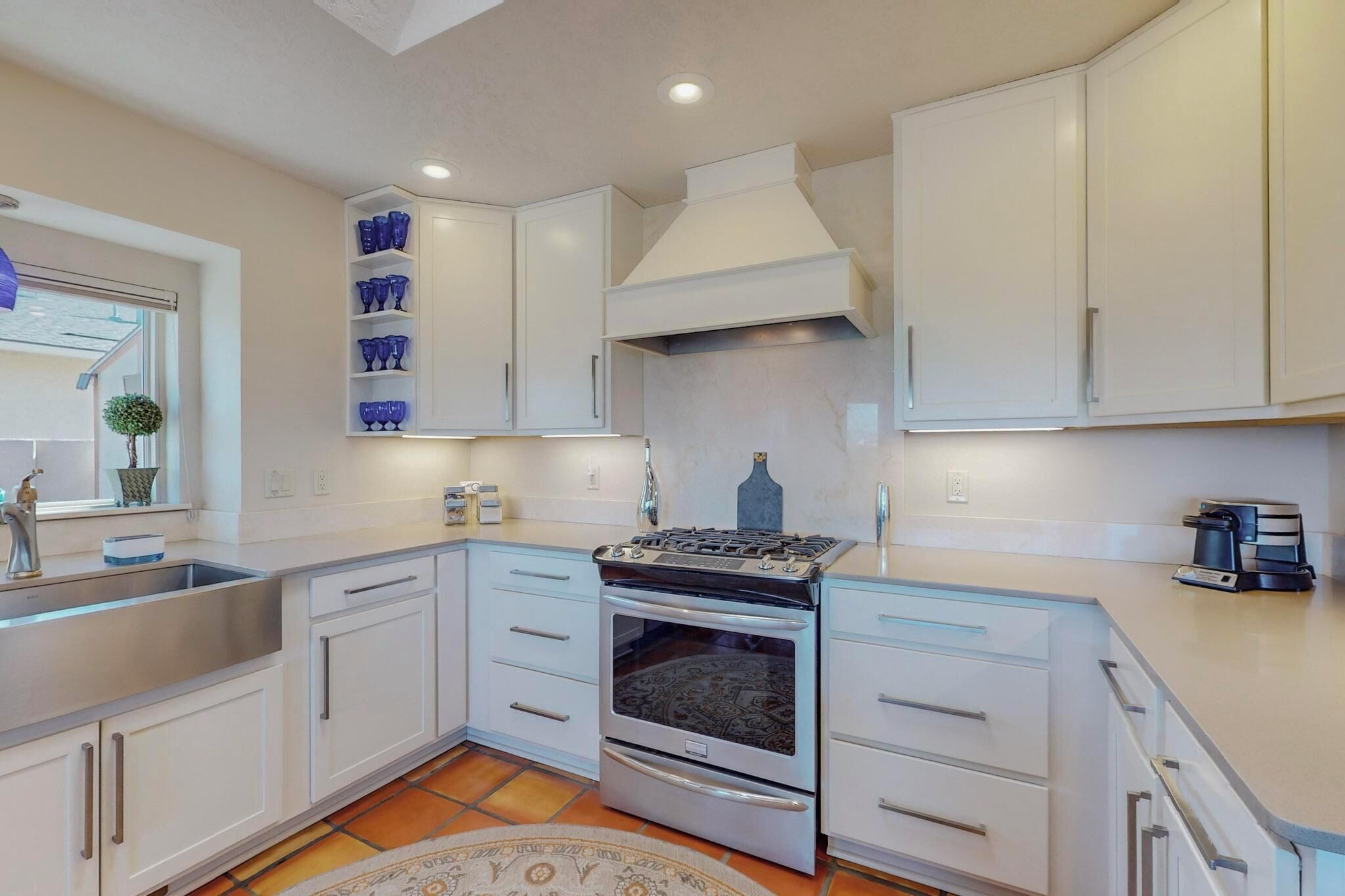 Una cocina moderna con armarios blancos, un lavamanos de acero inoxidable y un horno empotrado.