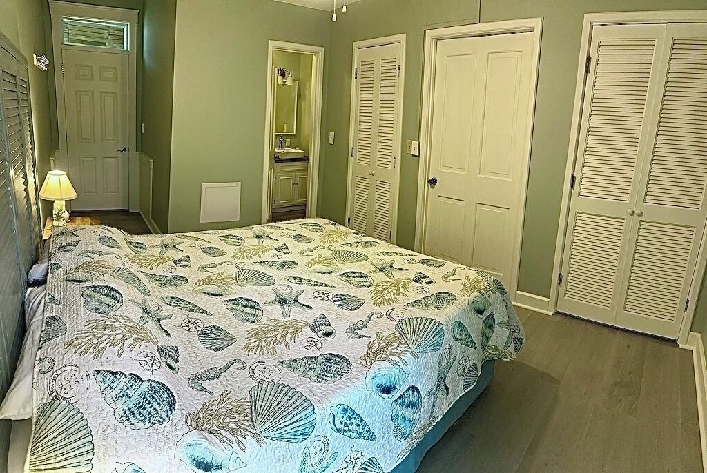 A bedroom with a bed, a nightstand, a dresser, a mirror, and two doors.