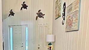 Een gang met een houten bank, een deur en wanddecoraties met onder andere zeeschildpadden en zeethema’s.