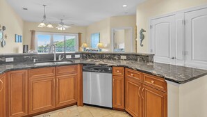 A kitchen with wooden cabinets, a dishwasher, and a marble countertop. - The Dunes: Ocean View Condo with Community Pool, Hot Tub, Beach Access (Oak Island)