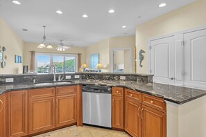 A kitchen with wooden cabinets, a dishwasher, and a marble countertop. - The Dunes: Ocean View Condo with Community Pool, Hot Tub, Beach Access (Oak Island)