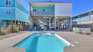 En swimmingpool med en solterrasse, omgivet af blå og hvide bygninger, samt udendørs møbler.