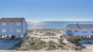 Et hus ved stranden med en sandstrand foran, en klar himmel og havet i baggrunden.
