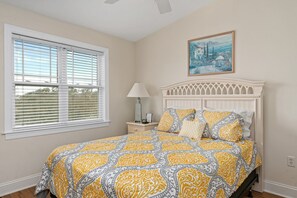 A bedroom with a large bed, a nightstand, a lamp, and a window with blinds.
