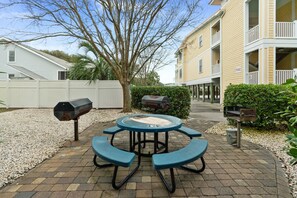 A patio with a round table and benches, surrounded by a white fence, a barbecue grill, and a mailbox.