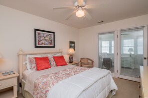 A bedroom with a bed, a ceiling fan, a nightstand, a chair, and a door with blinds. - Sweet Retreat: Oceanfront Home with Private Walkway to the Beach (Oak Island)