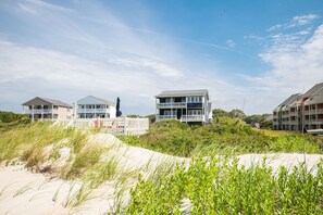 A beachfront property with multiple buildings, including a large house with a balcony and a smaller structure. - Sweet Retreat: Oceanfront Home with Private Walkway to the Beach (Oak Island)