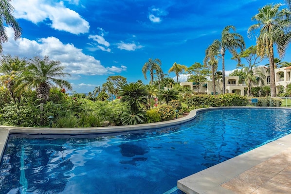 Relax by the resort's pool surrounded by lush greenery and Mediterranean-style buildings.