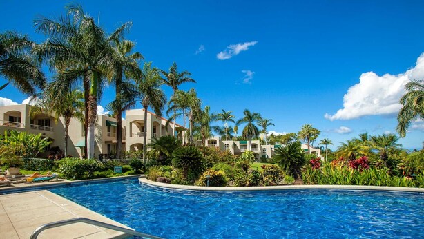 Una piscina con agua azul cristalina, rodeada de palmeras y un edificio con balcones.