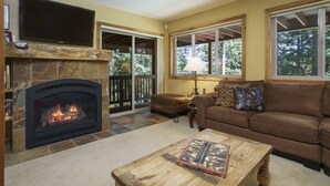 A living room with a fireplace, a brown leather sofa, a coffee table with a book, and a TV mounted above the fireplace. - Blue Bend Beauty | Comfort & Privacy with Postcard Views & Private Hot Tub (Breckenridge)