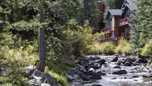 A lodge with a wooden exterior, multiple balconies, and a river running through the property surrounded by dense forest. - Blue Bend Beauty | Comfort & Privacy with Postcard Views & Private Hot Tub (Breckenridge)