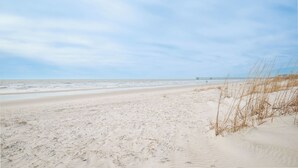 Una playa arenosa con un muelle a lo lejos.