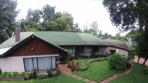 A two-story house with a green roof, a front porch, and a well-maintained lawn. - Cana Guest House (Harare)