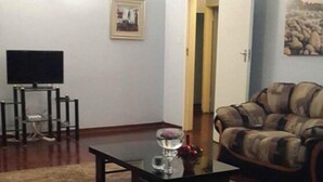 A living room with a coffee table, a sofa, a TV, and a door leading to another room. - Cana Guest House (Harare)
