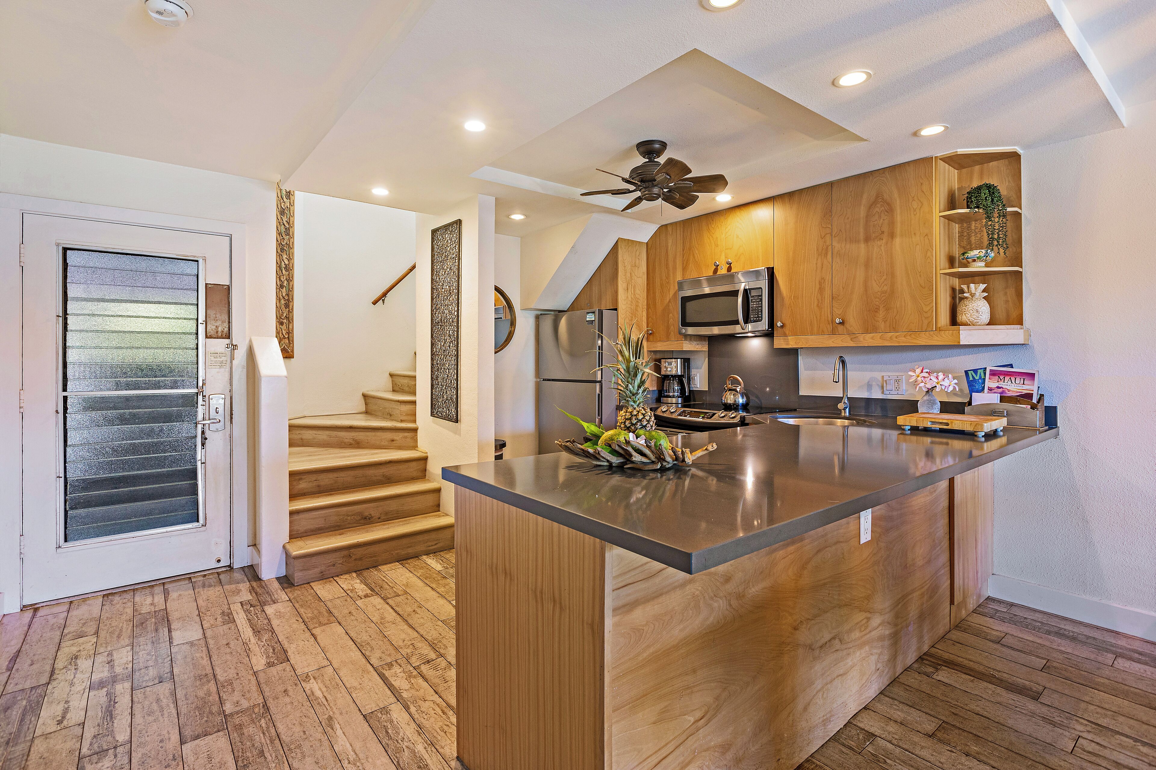 A modern kitchen with wooden cabinetry, a central island, stainless steel appliances, and a ceiling fan.